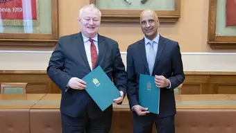 Na zdjęciu sygnatariusze umowy - stoją uśmiechnięci obok siebie, trzymając w dłoniach zielone teczki z dokumentami. Zdjęcie wykonane 