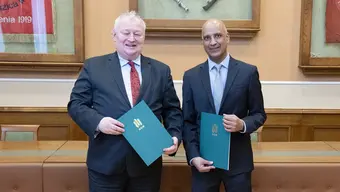 Image of two men wering suits holding folders, smiling and posing to the camera