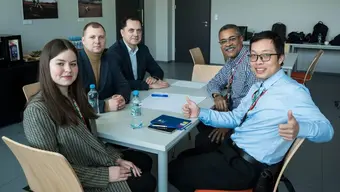 Image of five people sitting at a table looking in the direction of the photographer