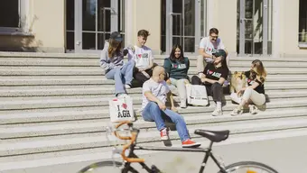 Students showcasing AGH University apparel and accessories on steps outside a university building.