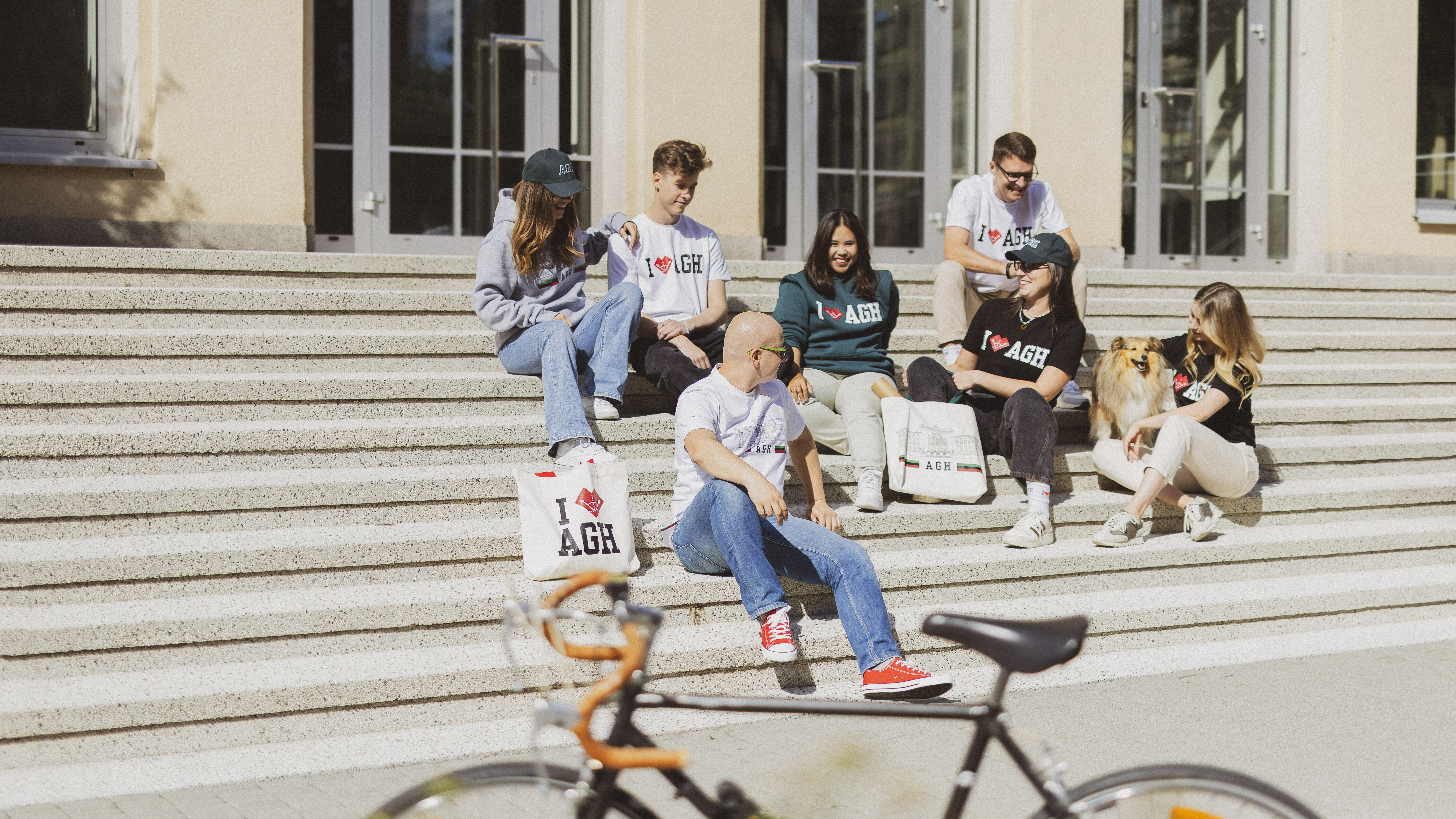 Students showcasing AGH University apparel and accessories on steps outside a university building.