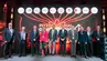 Group of formally dressed attendees posing on a stage at an international construction conference, with logos displayed on a large screen behind them.