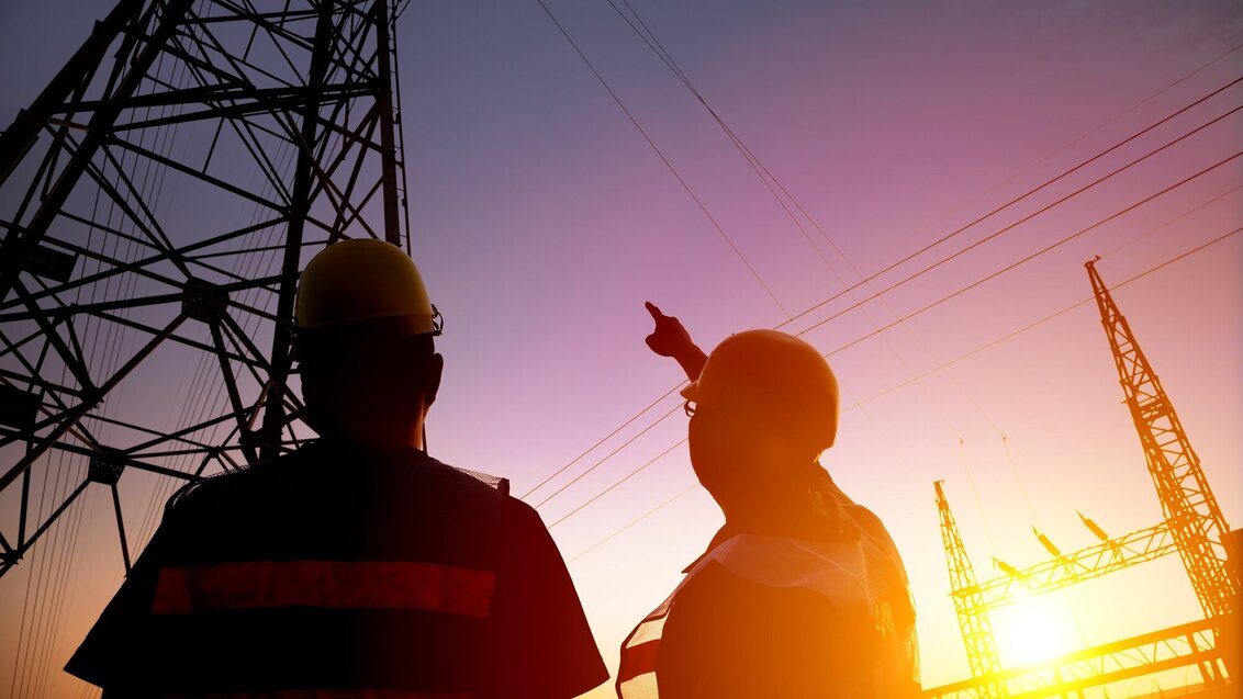 Image of two energy engineering looking up, one of them is pointing at an electricity pylon