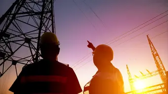 Image of two energy engineering looking up, one of them is pointing at an electricity pylon