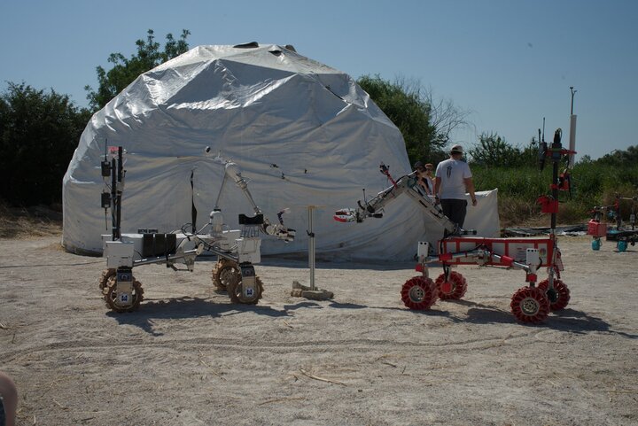 Two planetary rovers positioned opposite each other at the competition site. In the background is a dome simulating a space station.