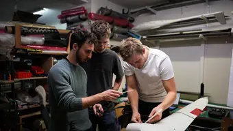 Three young men working on an unmanned aircraft in a workshop setting.