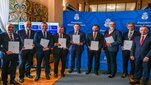 A group of officials standing indoors in front of a blue Krakow city backdrop, each holding a signed document following the signing of a letter of intent.