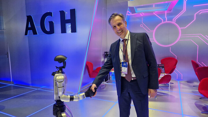 Uśmiechięty mężczyzna w uścisku dłoni z małym humanoidalnym robotem.
