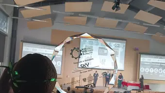 A photo of a glass statuette. A coconut next to it. In the background, a room filled with the participants of the competition gala.