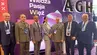 Six men and a woman in business and military attire posing in front of an AGH-branded backdrop.