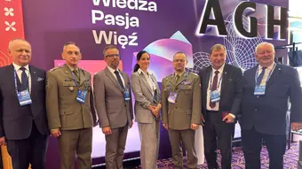 Six men and a woman in business and military attire posing in front of an AGH-branded backdrop.