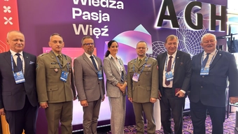 Sześciu mężczyn i jedna kobieta pozują do pamiątkowego zdjęcia. W tle kolorowa ścianka z emblematami AGH.