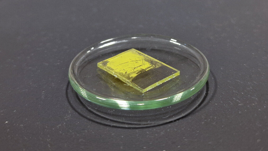 Mała przeźroczysta płytka pokryta cienką warstwą żółtego materiału
