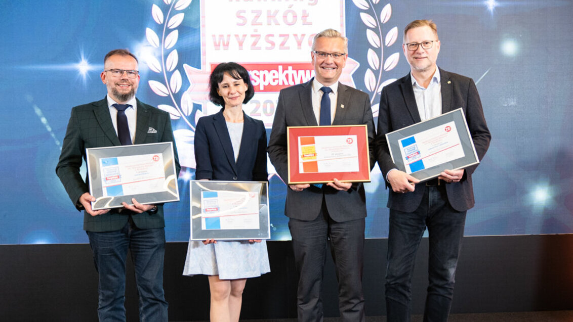 The photo shows three men and a woman standing in a row. They are holding diplomas certifying to their places in the ranking. Everyone is smiling. In the background, there is a logo of the "Perspektywy" University Ranking.