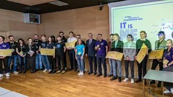 Image of the competition winners standing with their awards in front of a presentation with a logo of the competition