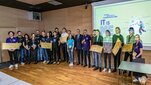 Image of the competition winners standing with their awards in front of a presentation with a logo of the competition