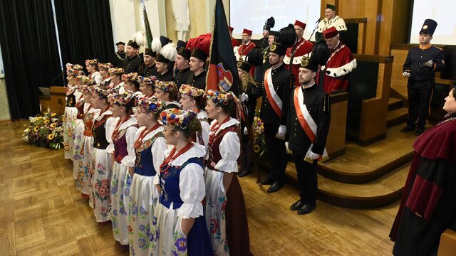 Academic ceremony with university representatives, flag bearers, and a folk ensemble.