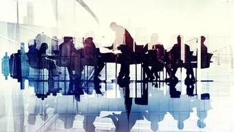 Grafika ilustracyjna przedstawiająca sylwetki ludzi siedzących przy stole i uczestniczących w spotkaniu.