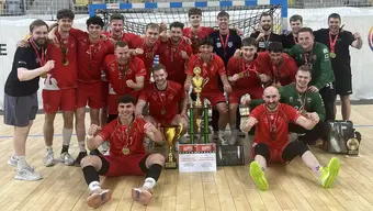 A group photograph of handball players in red, green, and black uniforms with gold medals on their necks and a gold cup in front of them.