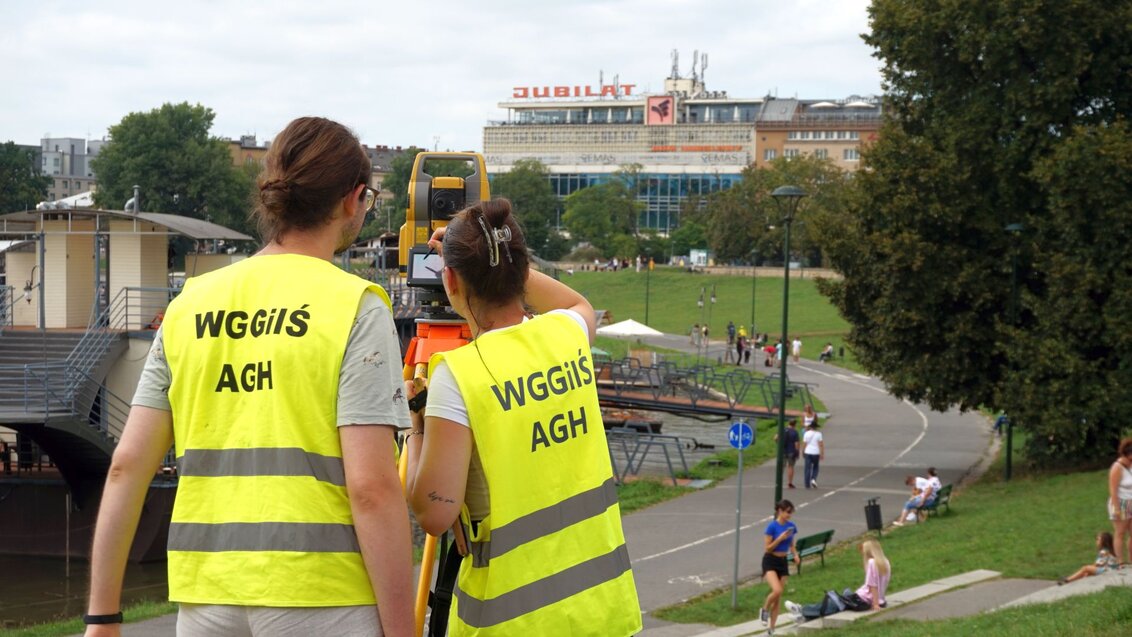 Two women in high-visibility vests using a geodetic tripod.