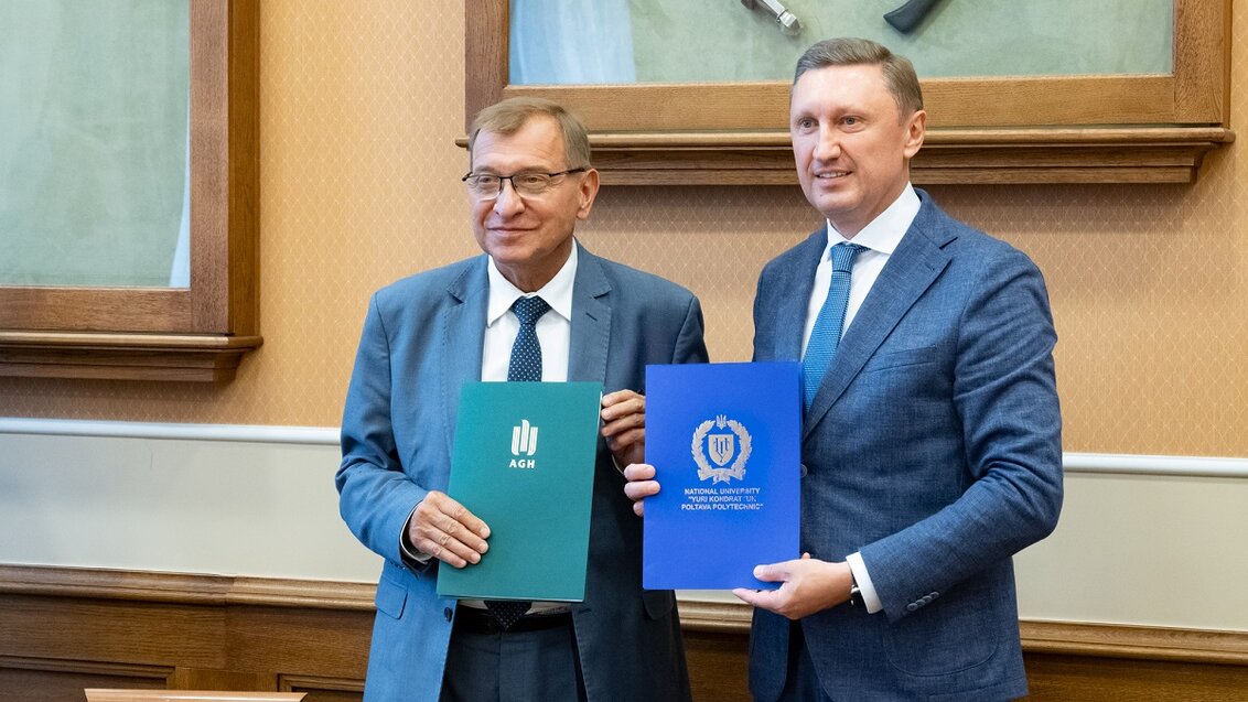 Two men (rectors of both universities) in suits posing for a photo next to each other. They are holding folders with the graphic symbols of their universities.