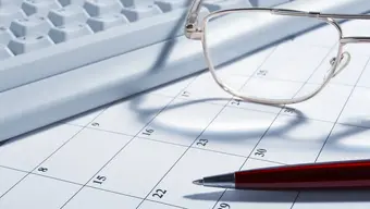 Zdjęcie ilustracyjne: biała klawiatura komputerowa, kartka z kalendarza, długopis, okulary.