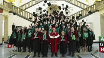Image of the AGH University alumni throwing their graduation caps up in the air and the university authorities holding the numbers making up the year 2024 in the front. They are standing in front of and on the stairs in the hall of the AGH University main building.