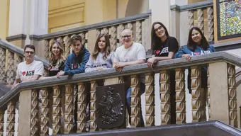 Grupa osób ubranych w odzież z logo AGH stoi przy balustradzie w reprezentacyjnym holu budynku głównego uczelni.