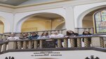 Grupa osób ubranych w odzież z logo AGH stoi przy balustradzie w reprezentacyjnym holu budynku głównego uczelni.