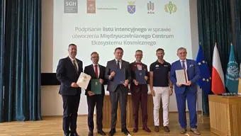Group of six people holding signed documents on a stage during the signing of a letter of intent to establish the Inter-University Space Ecosystem Center, with university logos and national flags in the background.