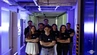 A group of young people in matching t-shirts in a purple-lit room.