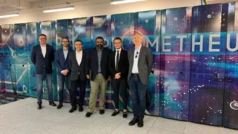 Six men in a row. Behind them is a colourful case of the Prometheus supercomputer.