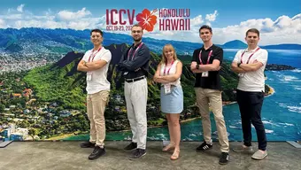 Grupa pięciu stojących osób na tle dużego banera konferencji, który przedstawia morskie wybrzeże