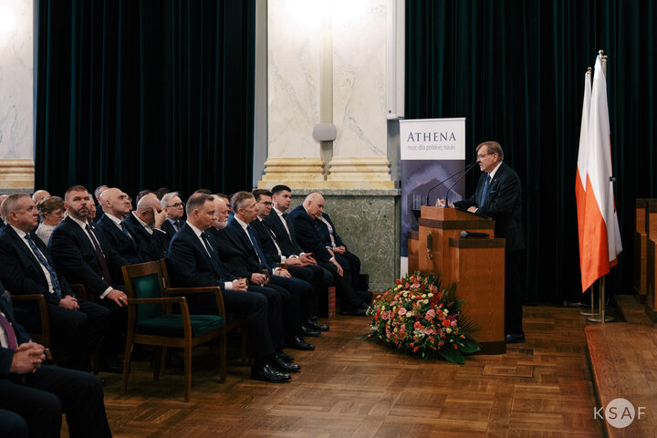 [A man standing at a lectern talking to the guests gathered in a representative hall.