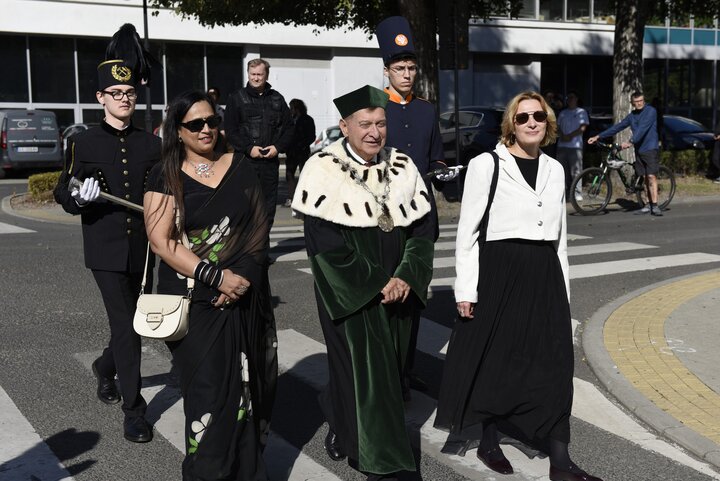 Participants of the inauguration ceremony walking across the campus, including a university official in ceremonial academic dress.