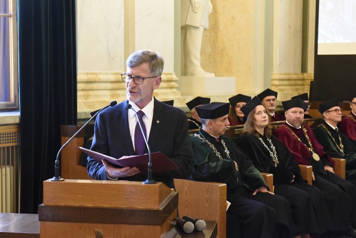 A man wearing glasses whilst giving a speech.