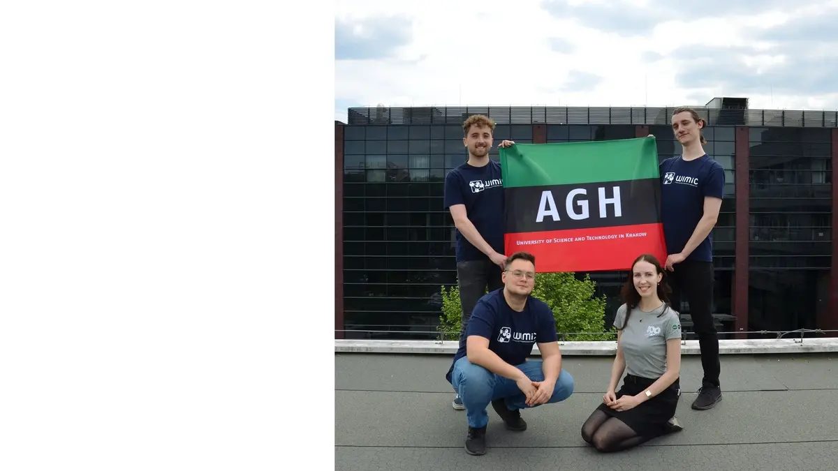 Członkowie Koła Naukowego Nucleus. Dwóch mężczyzn trzyma flagę AGH. Flaga składa się, patrząc od góry, z pasów zielonego, czarnego i czerwonego. Na czarnym pasie znajduje się biały napis „AGH”. Na czerwonym pasie u dołu znajduje się napis „University of Science and Technology in Cracov”. Pod flagą klęczą mężczyzna i kobieta.
