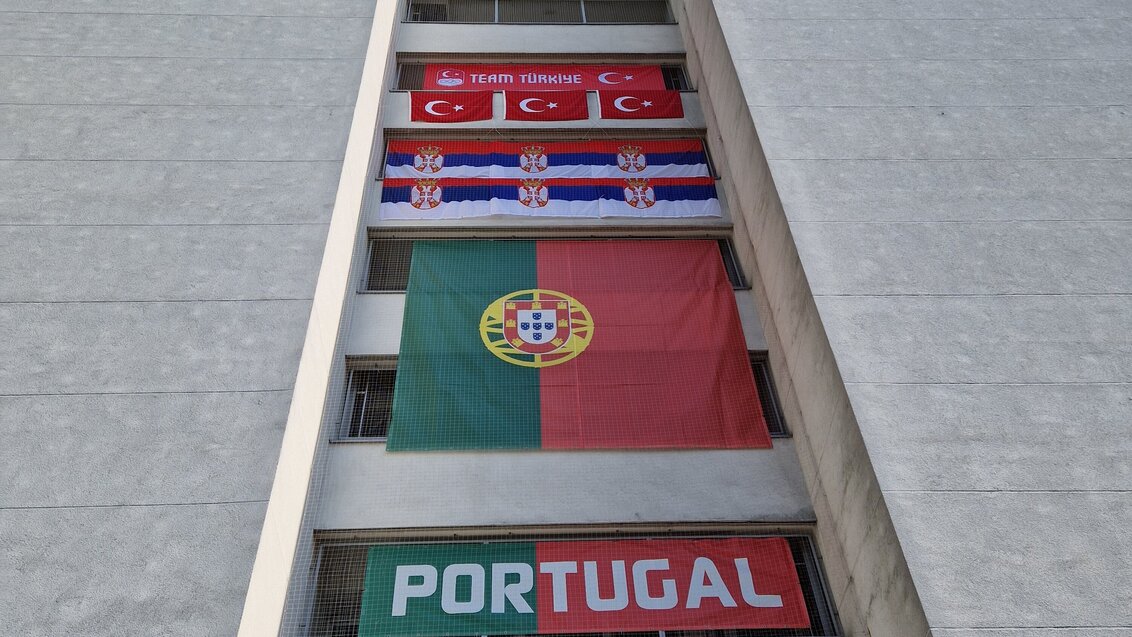 Na zdjęciu fragment ściany bocznej akademika. W oknach klatki schodowej rozwieszone flagi w barwach narodowych różnych państw.