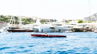 An image of Celka, a solar boat, sailing across a dock. A person in a red helmet is steering the boat.