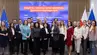 A group image of more than 20 people in business attire posing for a photograph in front of a large screen and Polish and EU flags.