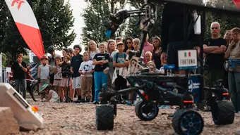 A four-wheeled robotic rover drives across a rocky obstacle course during the European Rover Challenge, surrounded by spectators standing behind barriers.