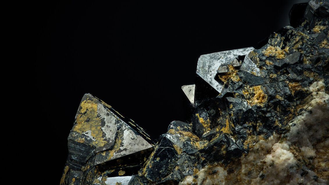 Kryształy o metalicznej barwie i stożkowym kształcie usytuowane na materiale skalnym