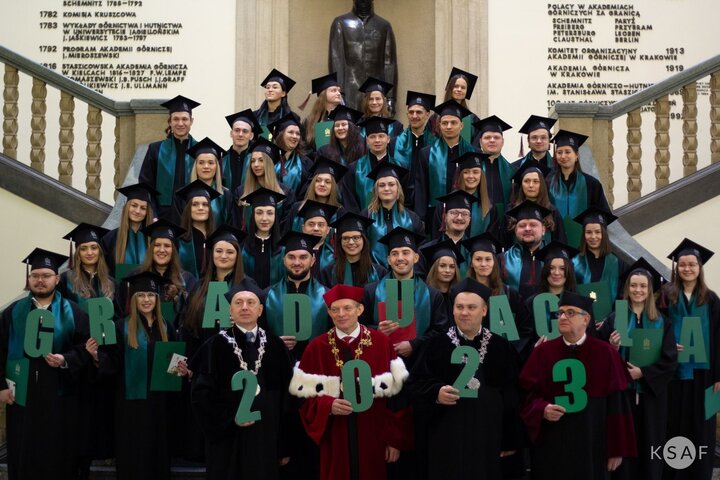 A commemorative photo of graduates and university authorities holding letters spelling "graduation" and numbers 2023, stading on the stairs in the main hall of the main AGH University building 