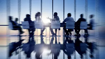 Grupa osób siedzących przy dużym stole konferencyjnym w nowoczesnej sali z panoramicznymi oknami.