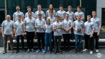 A group photo of people wearing matching polo shirts in front of a glass building.