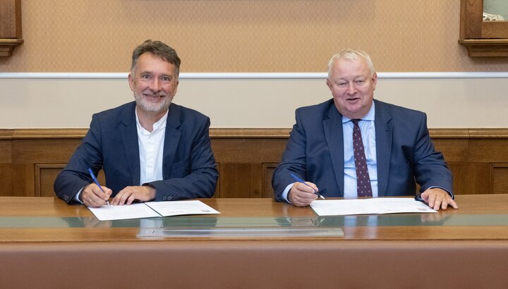 Two men smiling while signing documents in an official setting.