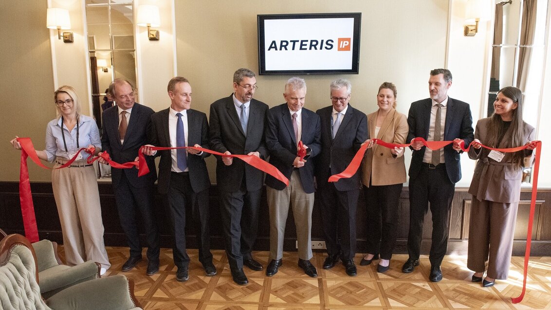 An image of a group of people cutting a long red ribbon in an elegant room with a screen behind them displaying the logo of Arteris