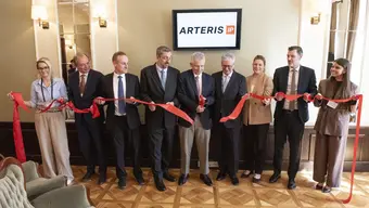 An image of a group of people cutting a long red ribbon in an elegant room with a screen behind them displaying the logo of Arteris