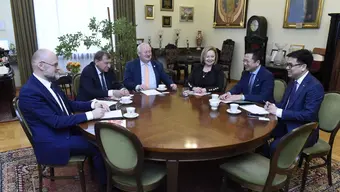 Zdjęcie osób uczestniczących w spotkaniu. Siedzą przy okrągłym stole w gabinecie rektorskim. Na stole filiżanki i dokumenty.