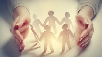 A pair of hands gently encircling a group of paper cut-out figures, representing connection, protection, and togetherness.